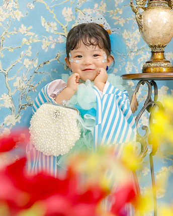 青い花柄の壁紙の前で笑う、縞柄の着物の男の子